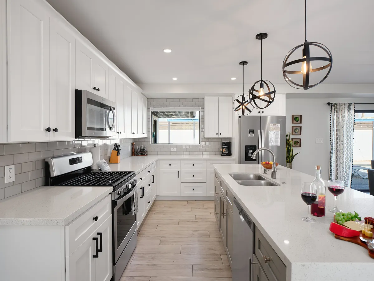 A modern kitchen with a central island, stainless steel appliances, pendant lights, and a variety of dining options. The scene is tidy and well-equipped, suggesting convenience and the presence of hotel-inspired starter kits for guests.