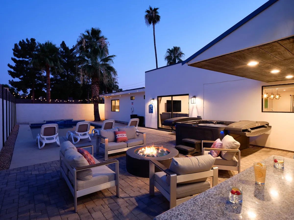 An inviting backyard scene at sunset featuring a sparkling pool, glowing fire pit surrounded by plush seating, and swaying palm trees. The atmosphere is cozy and intimate, perfect for evening gatherings and relaxation under the Arizona sky.