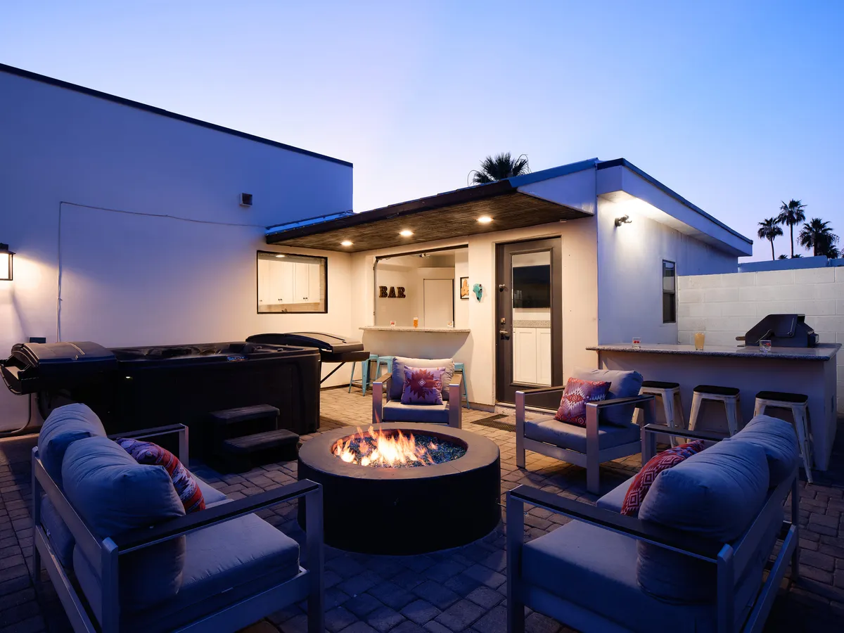 An inviting view of the fire pit area, outdoor bar, grill, and ample seating arranged for group gatherings. The lush landscaping frames the entertaining spaces, underlining the carefully curated, private-resort vibe of the backyard.