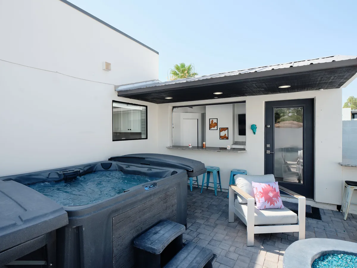 A tranquil backyard scene with a hot tub, a stylish bar counter, and an outdoor seating area. The area is surrounded by greenery and is perfect for relaxing in the hot tub or enjoying drinks and meals outside.