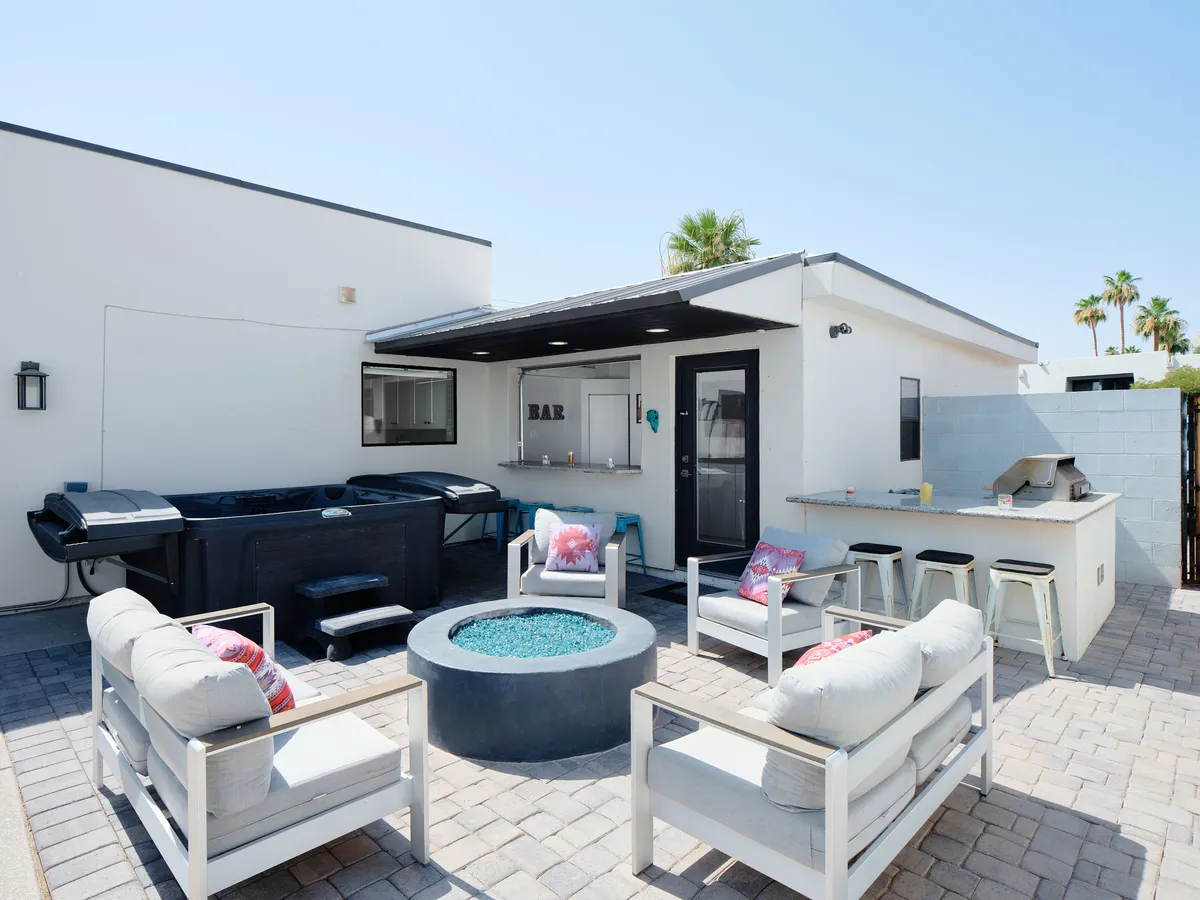 The image focuses on a cluster of backyard amenities: a bubbling hot tub, a fire pit surrounded by comfortable seating, and a well-equipped outdoor bar area. The mood is relaxed yet social, perfect for entertaining or unwinding at the end of the day.