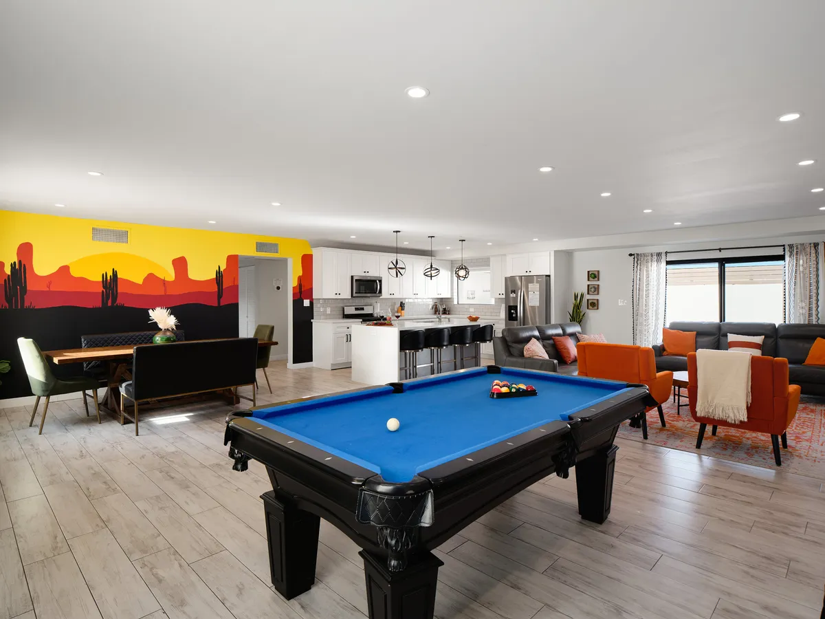 This image showcases the open-concept core of the property, featuring a pool table at the center, a comfortable seating area, colorful mural, and an adjacent dining area. The arrangement encourages social interaction, game nights, and communal dining in a lively, elegant setting.