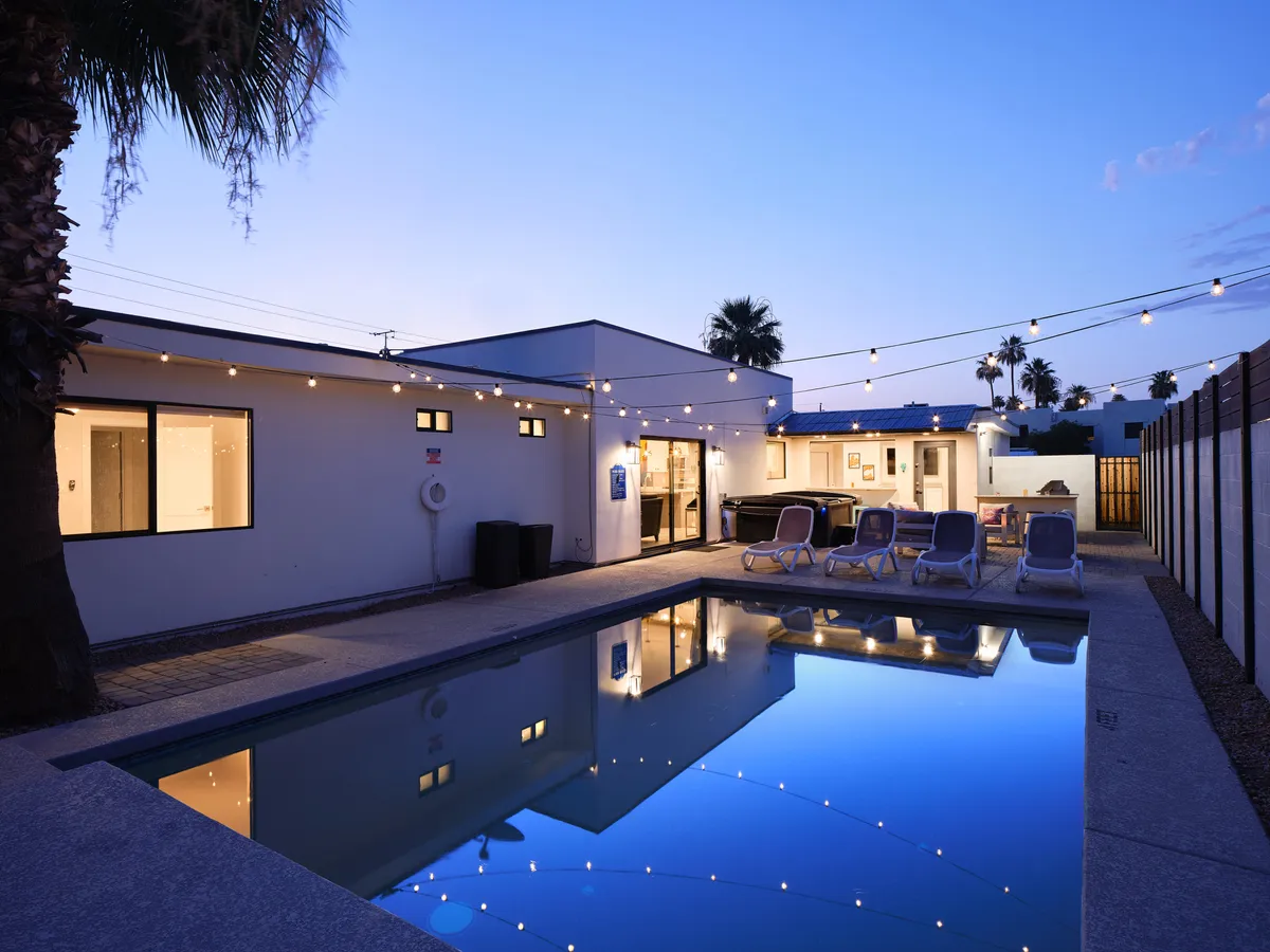 This image captures the sparkling swimming pool as dusk approaches, with string lights twinkling overhead and a cozy outdoor seating area placed poolside. The sky is painted with sunset hues, and the relaxed setup invites guests to swim, socialize, or savor a quiet moment by the water.