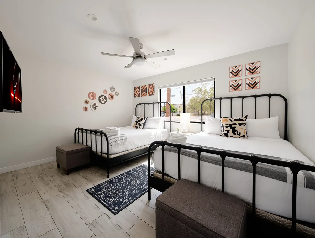 A spacious bedroom with multiple beds, each adorned with stylish linens and decorative pillows. Natural light streams through the window, and a TV is mounted on the wall, providing private downtime. The room is designed to accommodate different guest configurations, perfect for families or groups.
