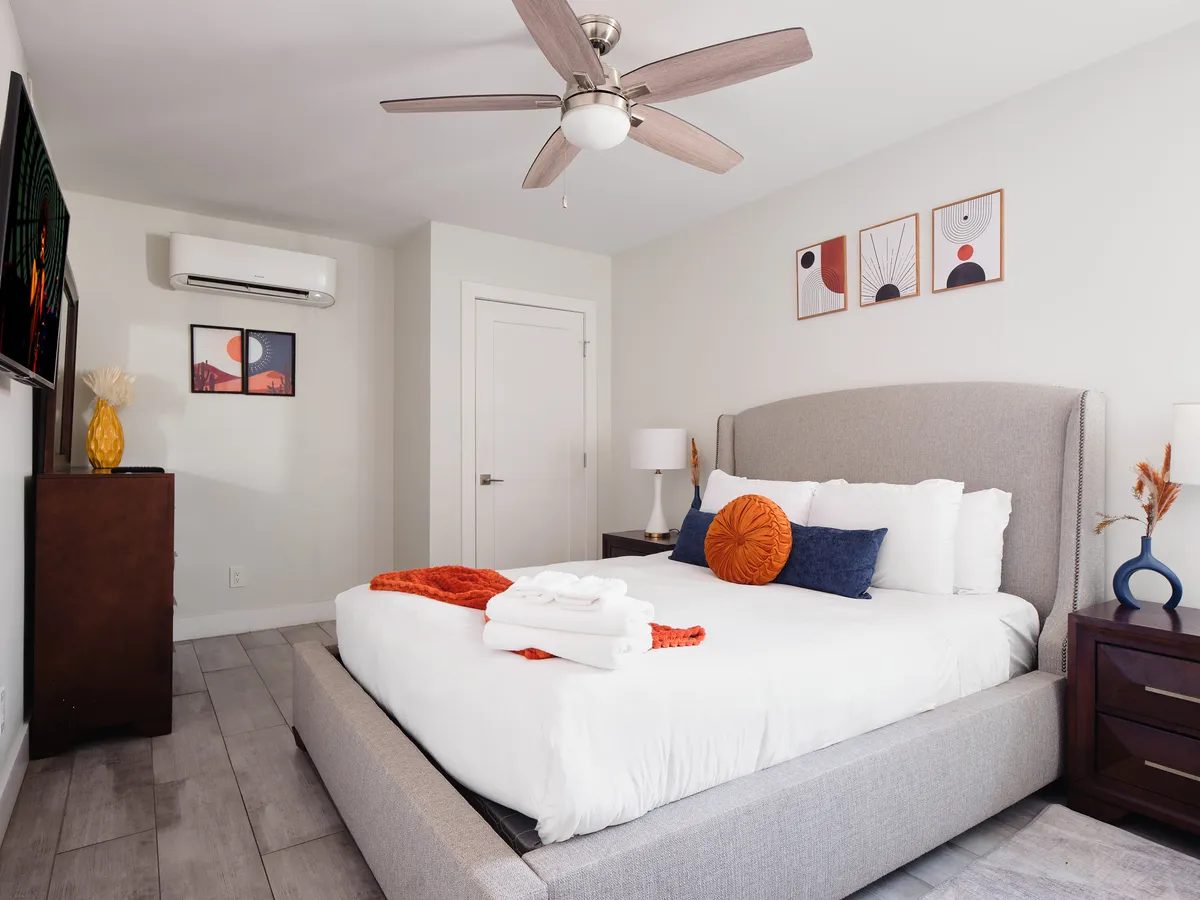 A serene bedroom featuring a king-size bed with colorful accent pillows, tasteful wall art above the headboard, a nightstand with a lamp, and soft, welcoming lighting. The space feels spacious and inviting, ideal for restful nights or enjoying quiet moments.